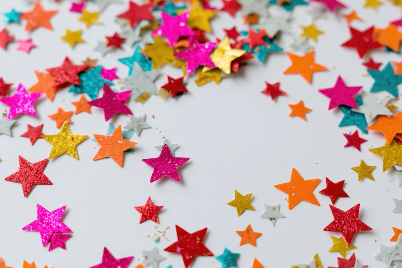 Scattered star-shaped confetti pieces in various colors and sizes on a white surface