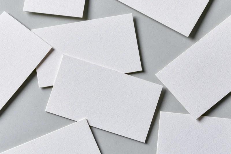 Blank white textured business cards scattered and overlapping on a gray surface