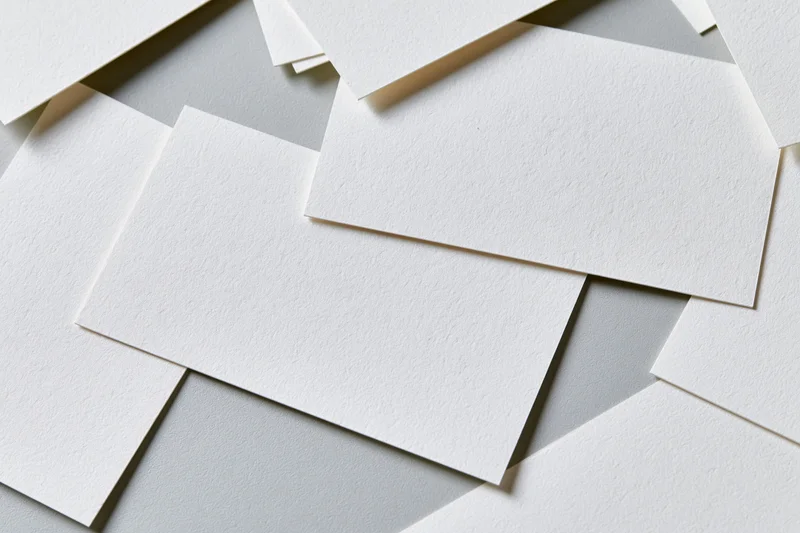 Blank white textured business cards scattered and overlapping on a light gray surface