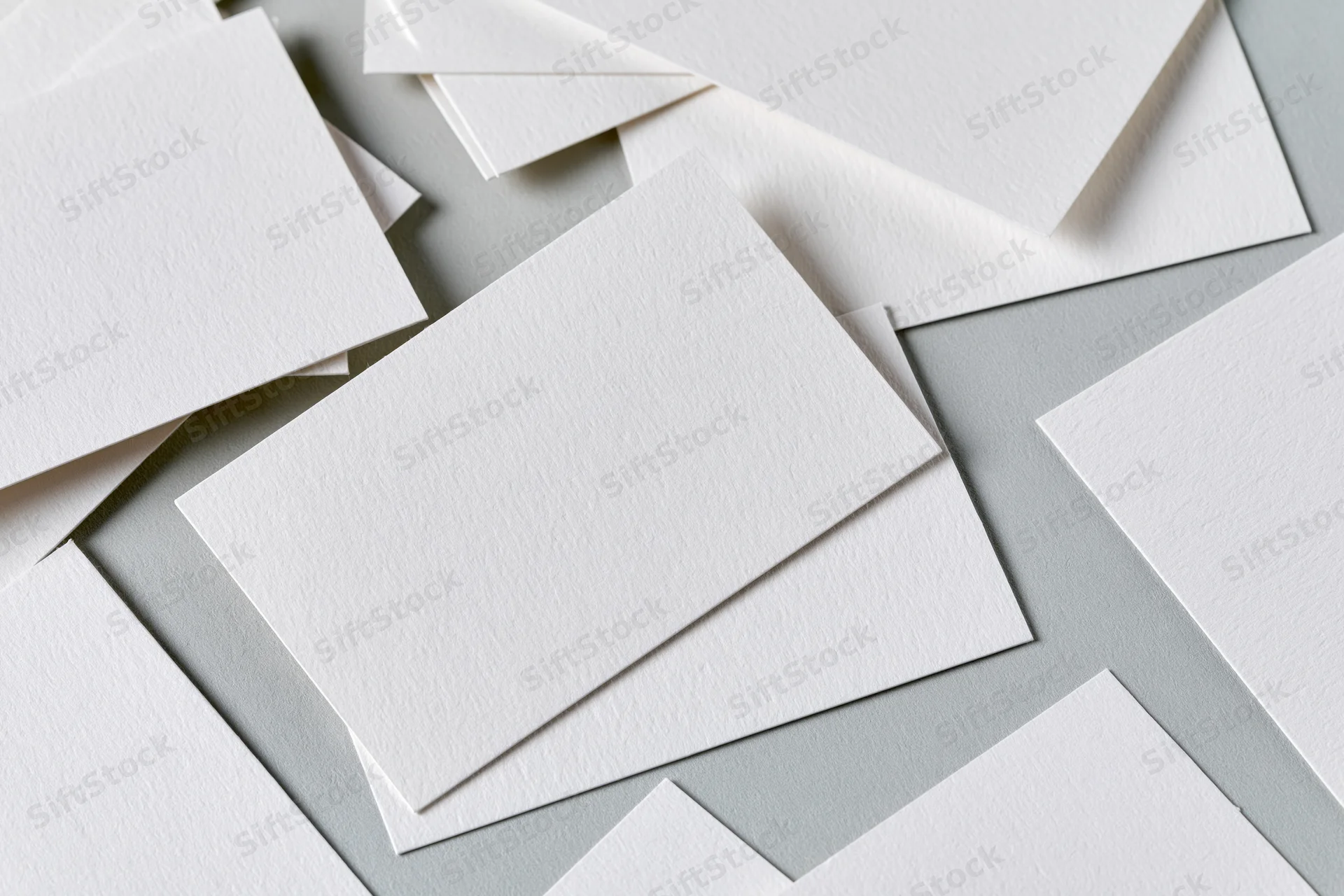 Blank white textured business cards scattered and overlapping on a gray surface