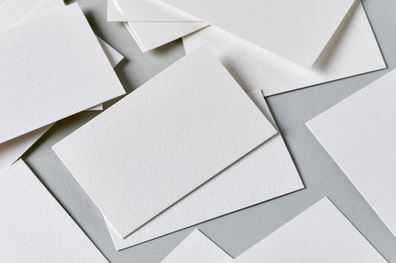 Blank white textured business cards scattered and overlapping on a gray surface
