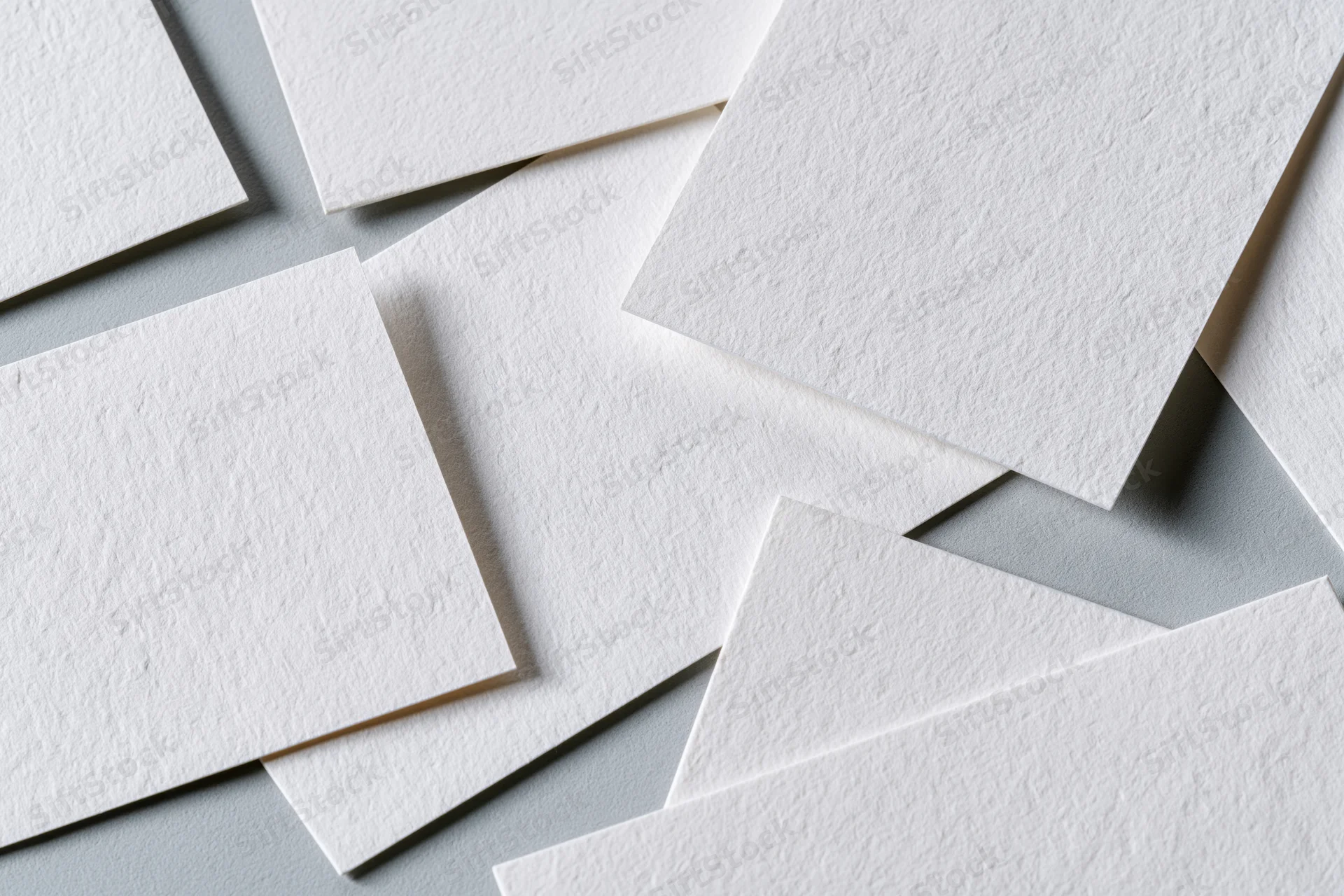 Blank white textured business cards scattered and overlapping on a gray surface