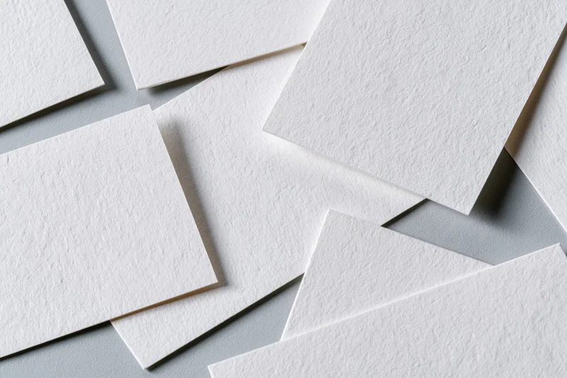 Blank white textured business cards scattered and overlapping on a gray surface
