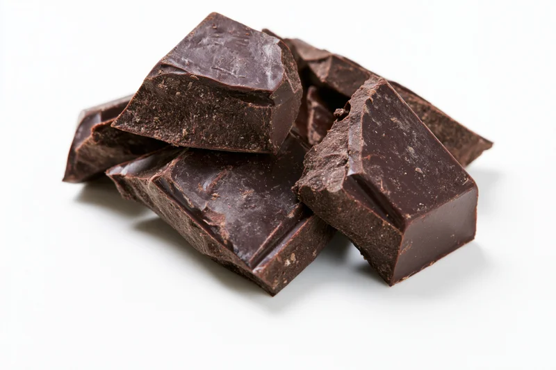 Broken dark chocolate chunks stacked on white background