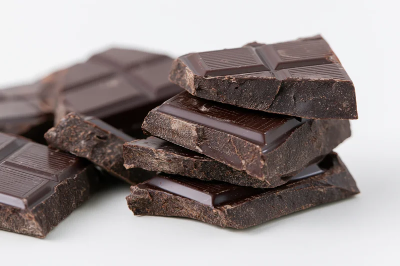 Broken dark chocolate pieces stacked and scattered on white background