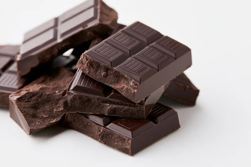 Broken dark chocolate pieces stacked and scattered on white background