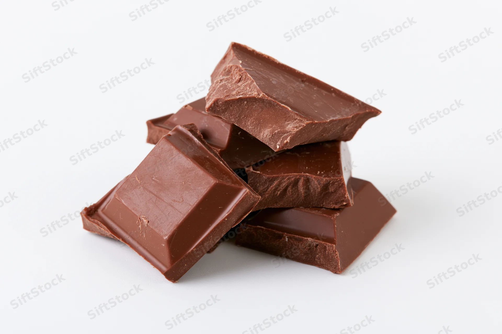 Broken milk chocolate bar pieces stacked and scattered on white background