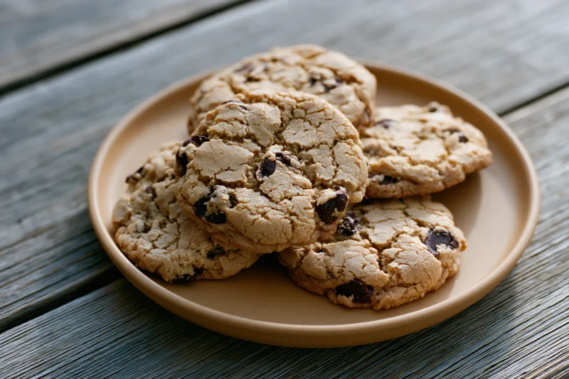 Chocolate chip cookies piled on a tan ceramic plate on a wooden table
