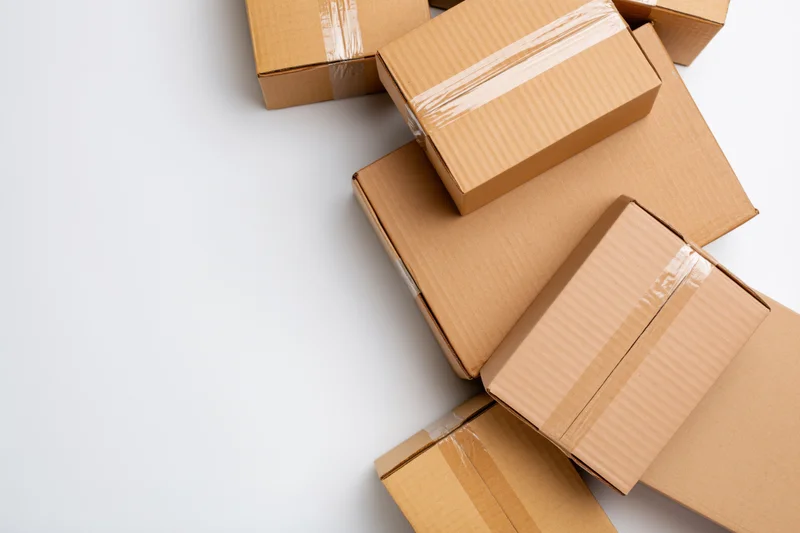 Closed cardboard shipping boxes of various sizes stacked on white surface with copyspace