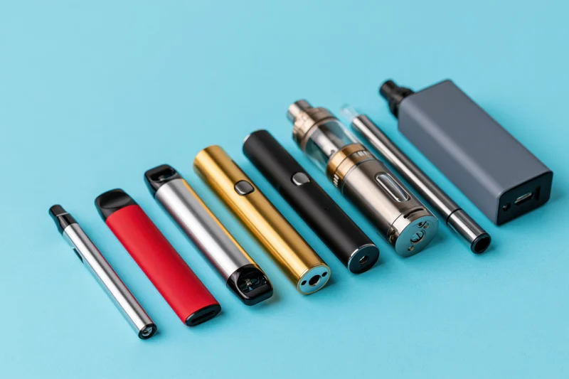 Various vaping devices and e-cigarettes arranged in a loose diagonal line on a blue background
