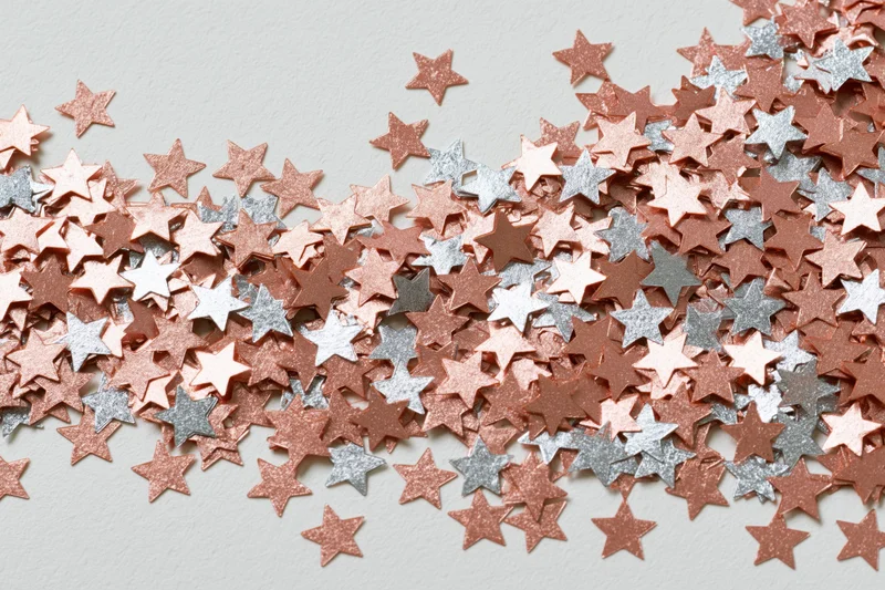 Metallic star-shaped confetti scattered across a white surface with copyspace