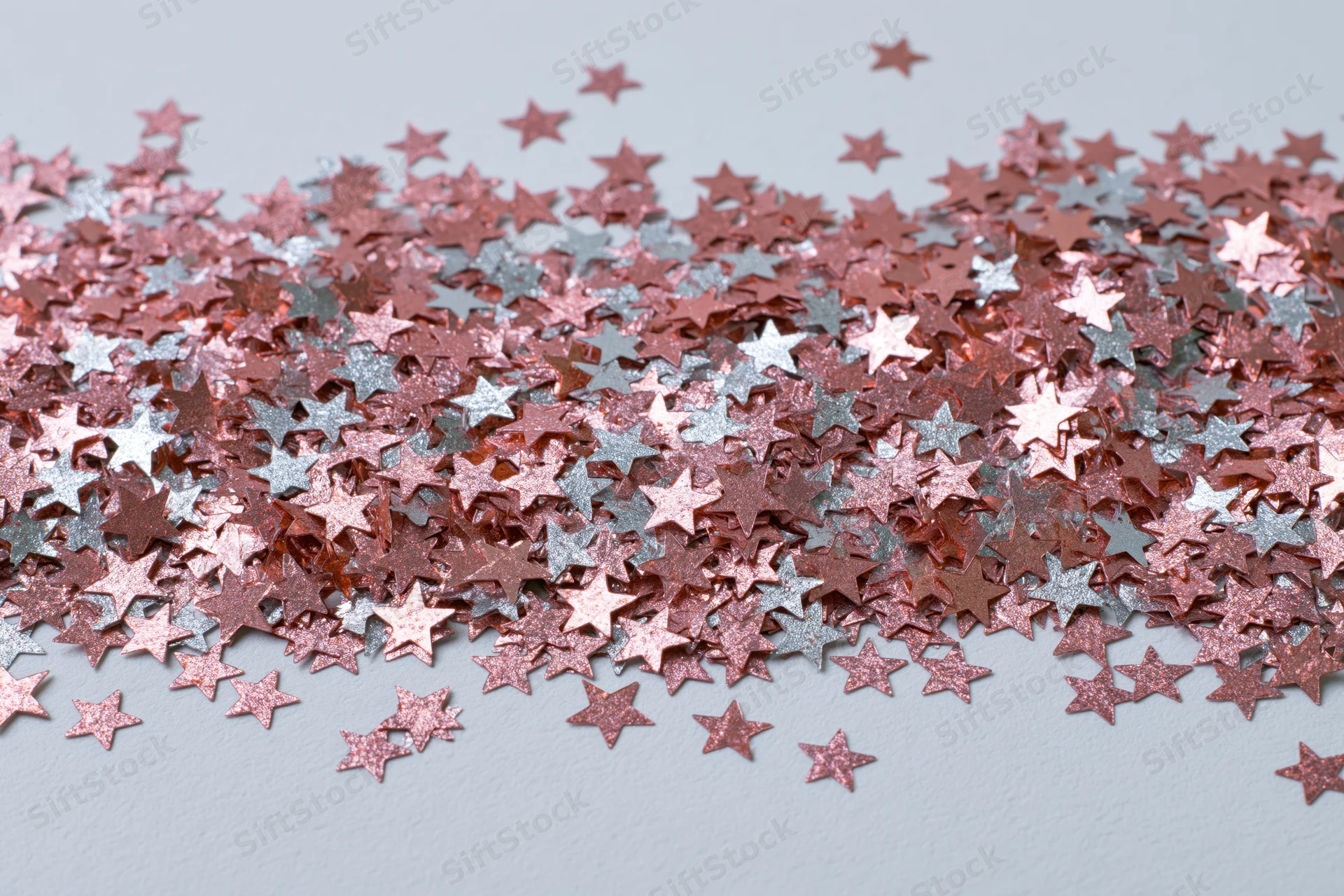 Metallic star-shaped confetti scattered across a light surface in a dense pile with copyspace at the bottom