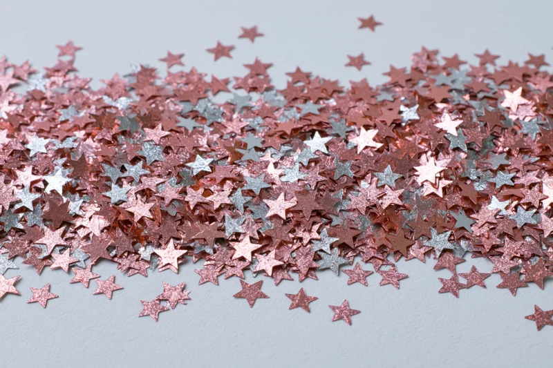 Metallic star-shaped confetti scattered across a light surface in a dense pile with copyspace at the bottom