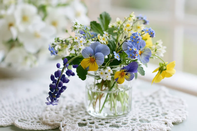 Small mixed wildflower bouquet in a clear glass jar on a lace doily on a table