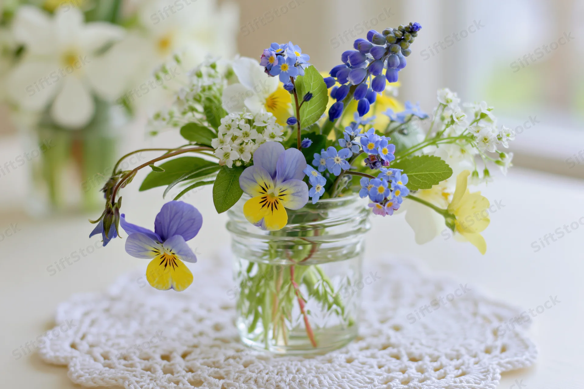 Small mixed wildflower bouquet in a clear glass jar on a crocheted doily on a table