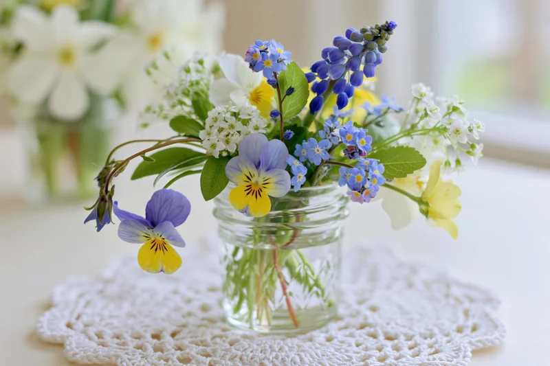 Small mixed wildflower bouquet in a clear glass jar on a crocheted doily on a table