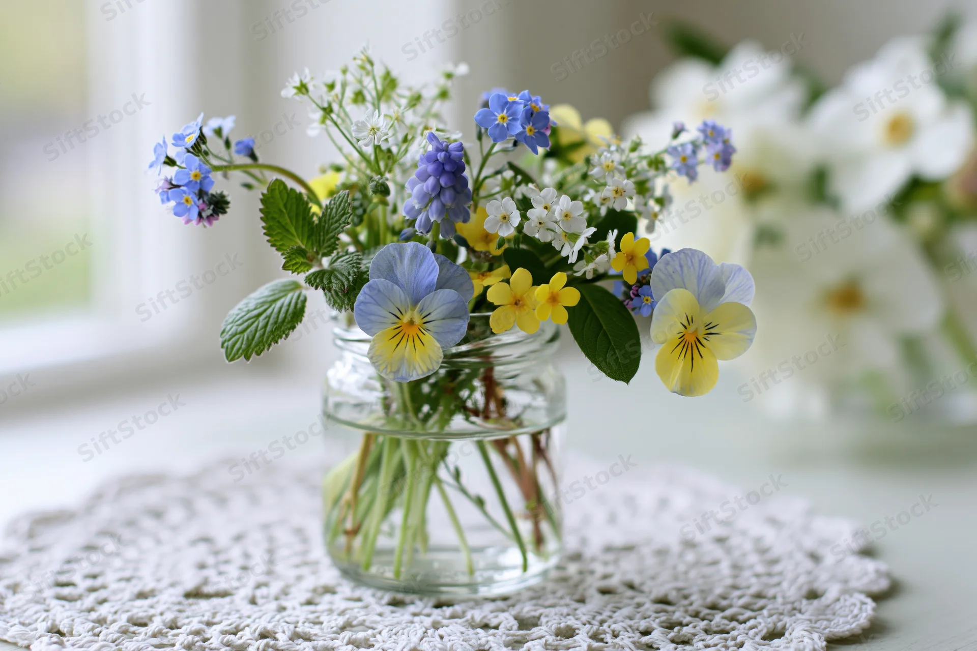Small mixed wildflower bouquet in a clear glass jar on a white lace doily on a table