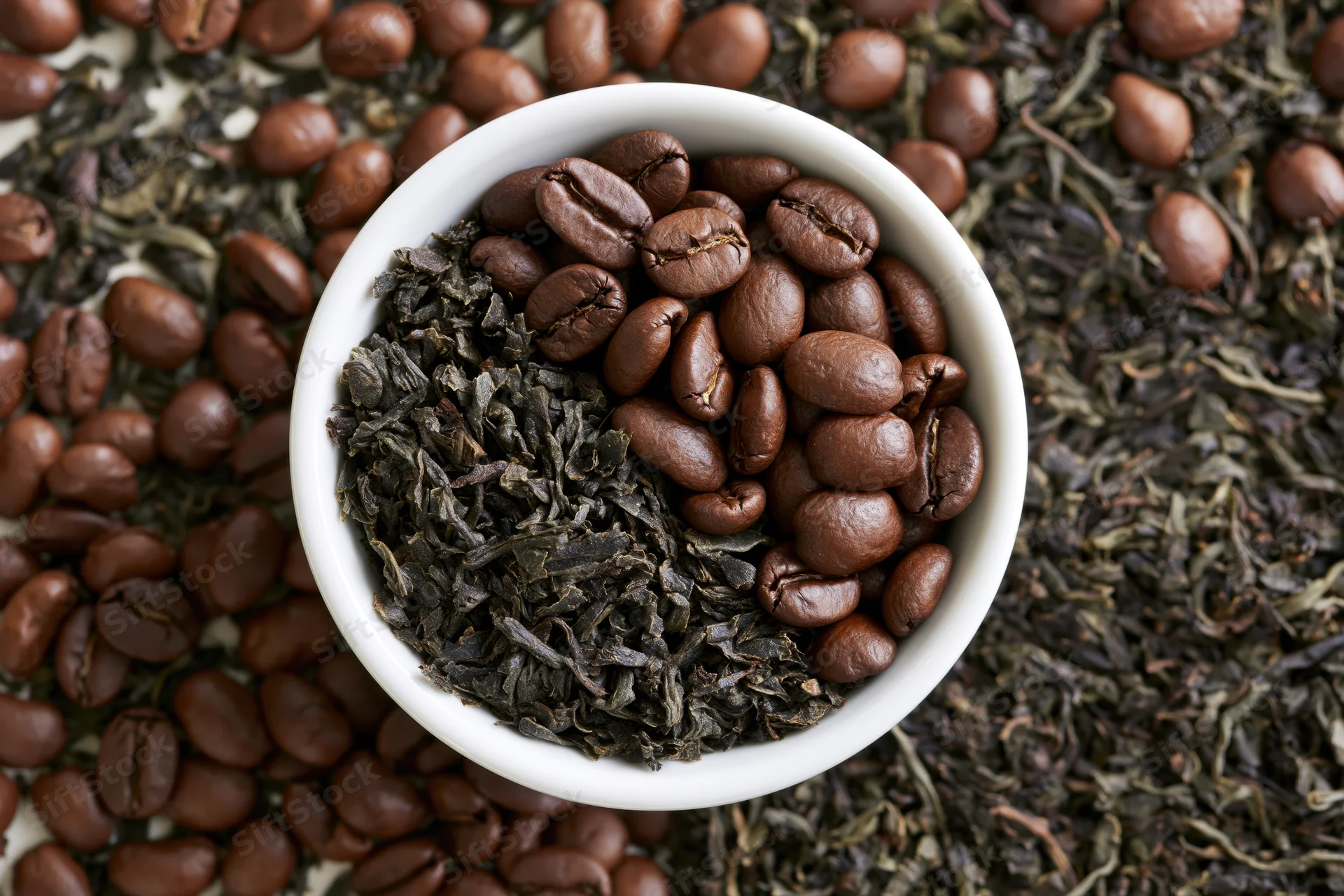 White ceramic bowl filled with roasted coffee beans and dried tea leaves, arranged on a scattered bed of beans and leaves