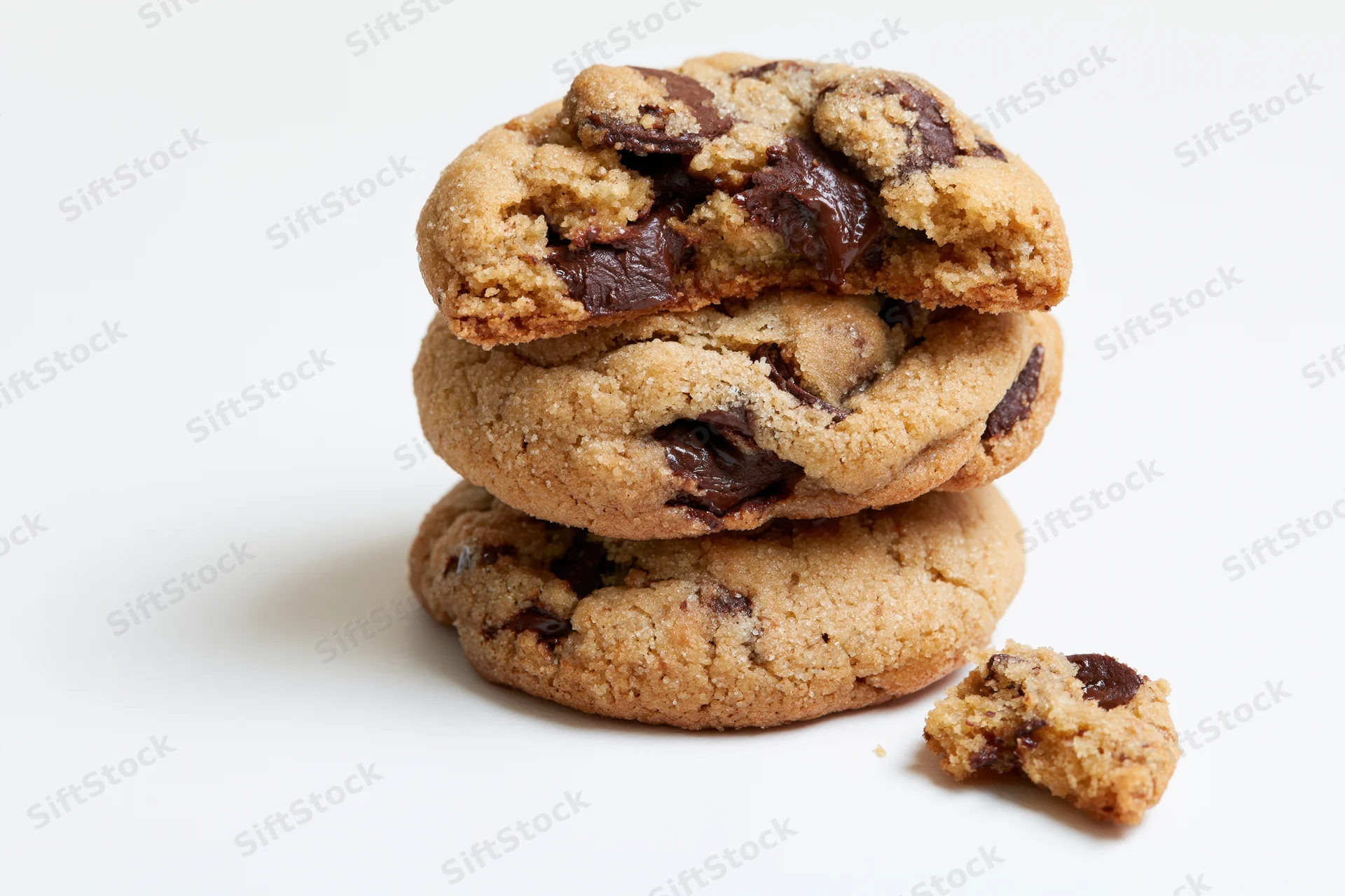 Stack of three chocolate chip cookies on white background with one broken piece beside