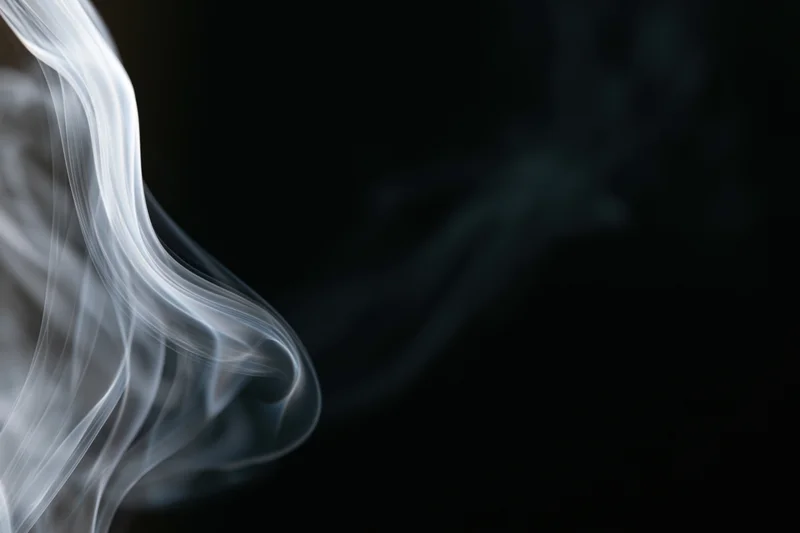 Thin wisp of white smoke curling upward against a dark background