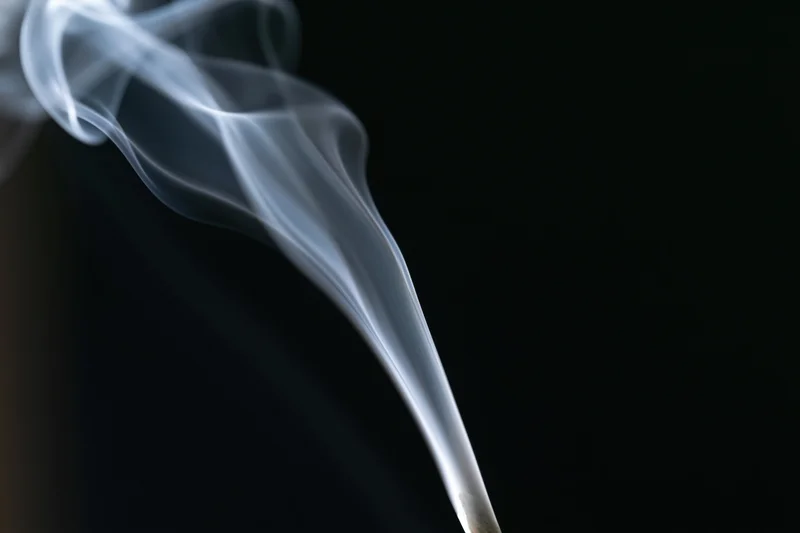 Thin wisp of white smoke rising and curling upward against a black background