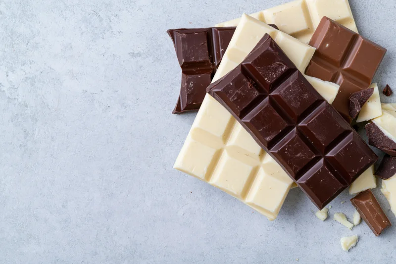 Overlapping dark white and milk chocolate bars arranged on a gray textured surface