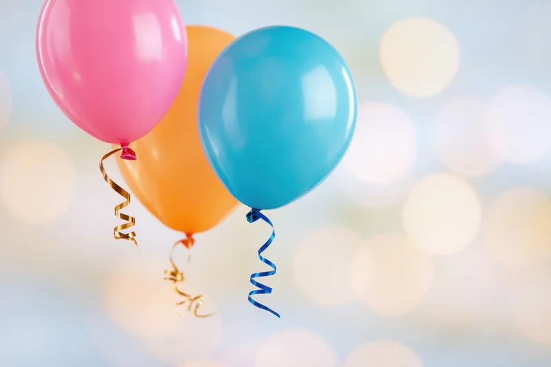 Three colorful latex party balloons floating against a blurred bokeh background with ribbons attached