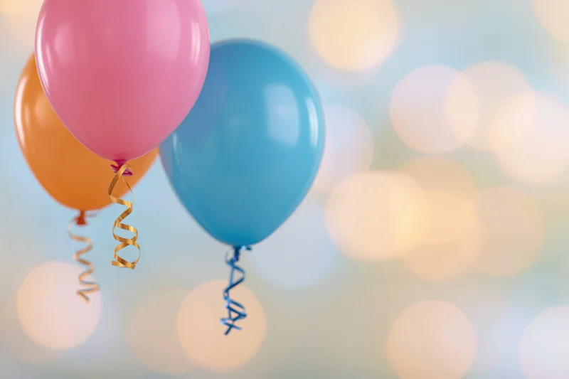 Three colorful latex party balloons floating against a soft bokeh background with copyspace