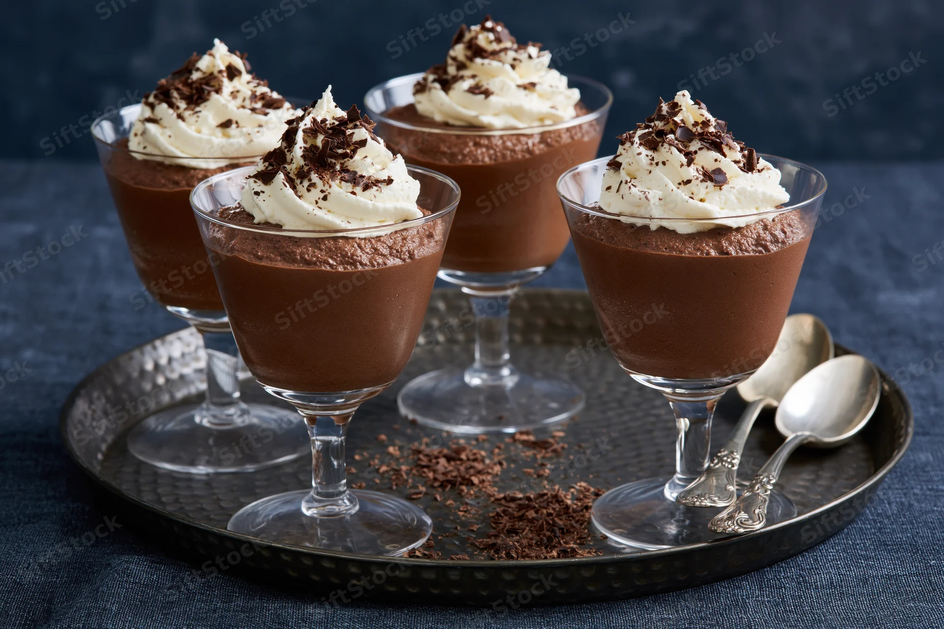 Chocolate mousse desserts in stemmed glasses topped with whipped cream and chocolate shavings on a silver tray with spoons