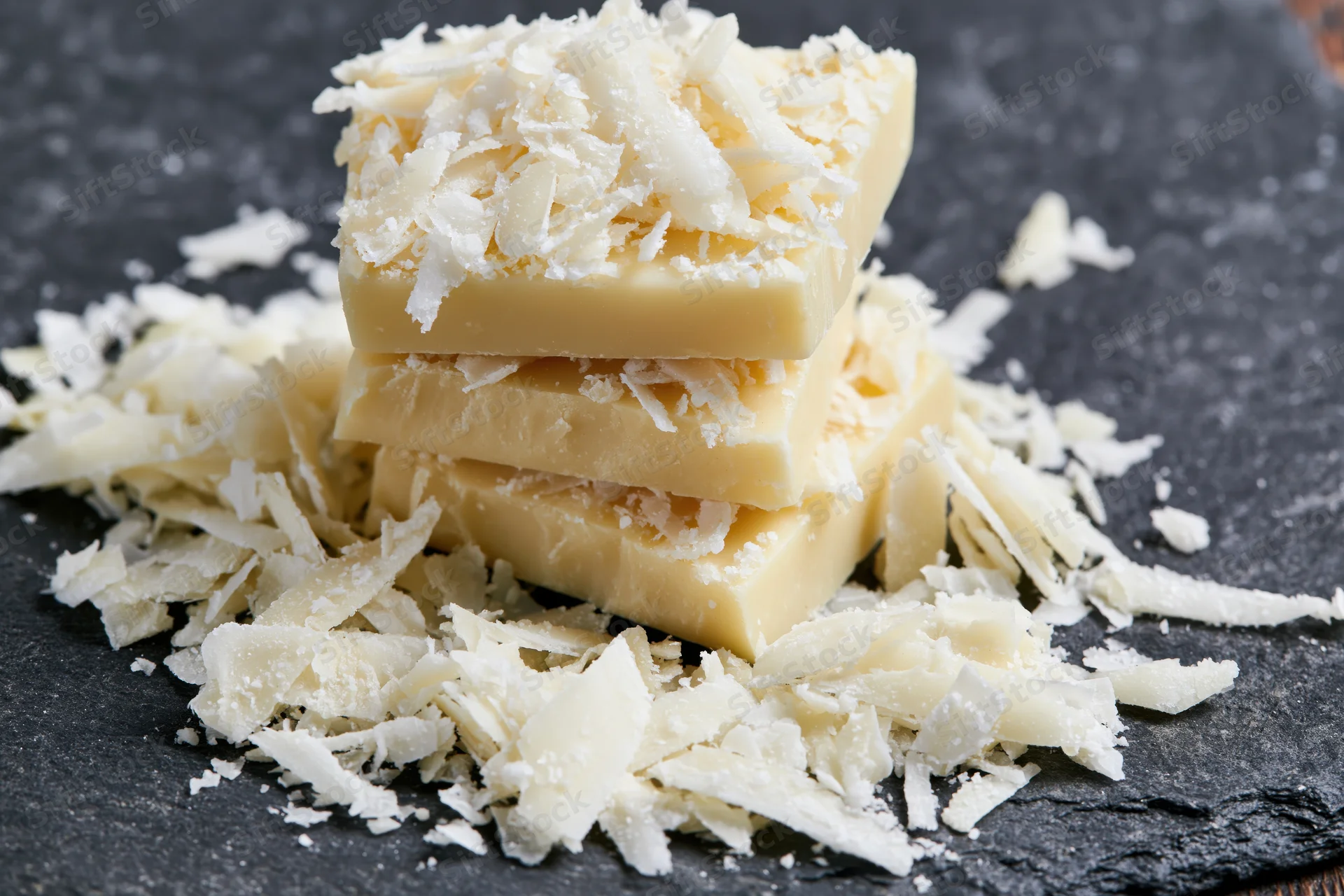 Three stacked white chocolate bars topped with shaved coconut on a dark slate surface
