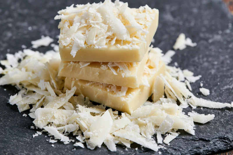 Three stacked white chocolate bars topped with shaved coconut on a dark slate surface