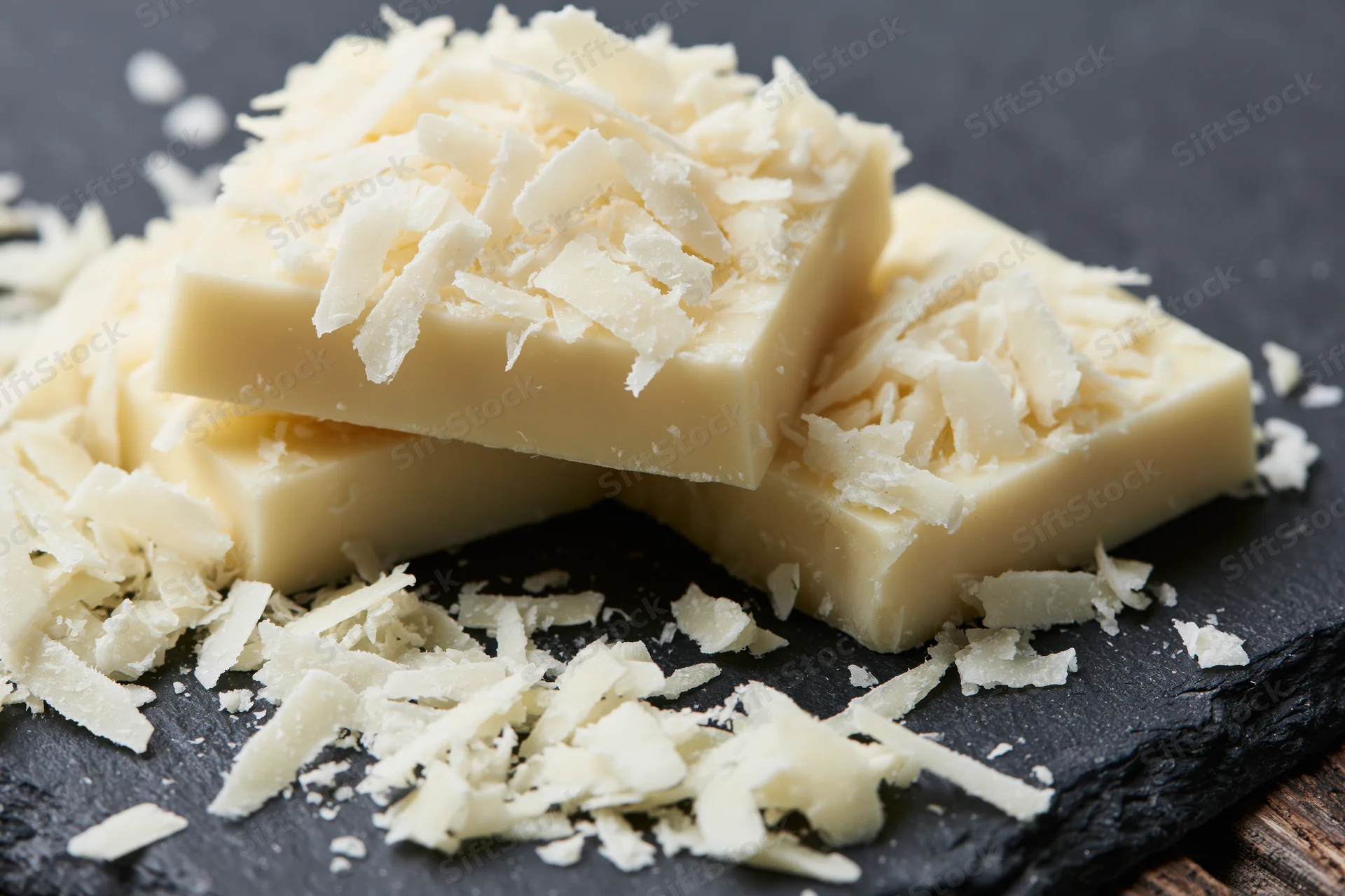 Stacked white chocolate blocks topped with shaved coconut on dark slate surface