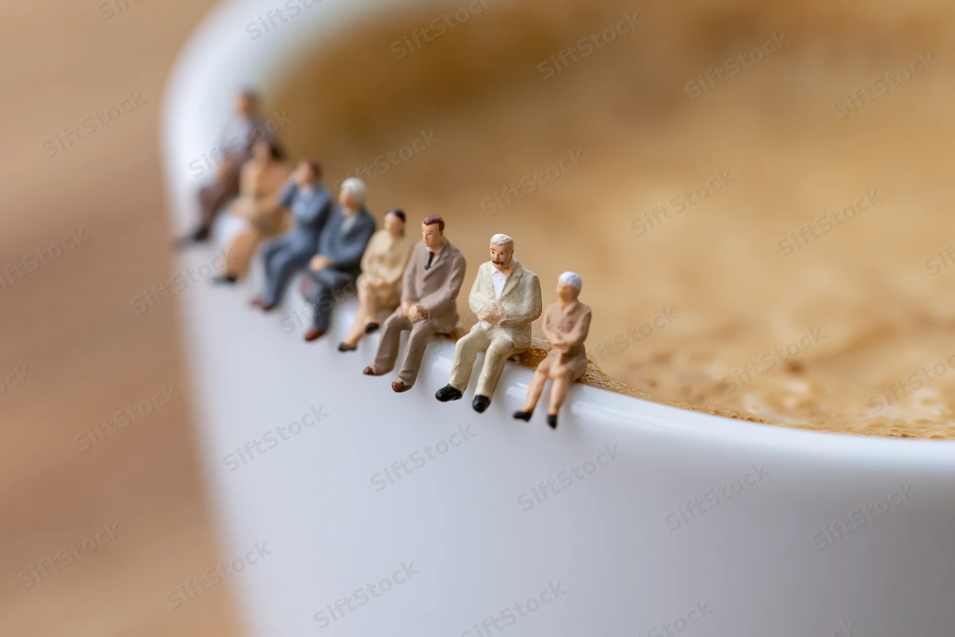 Miniature businesspeople seated in a row along the edge of a white coffee cup