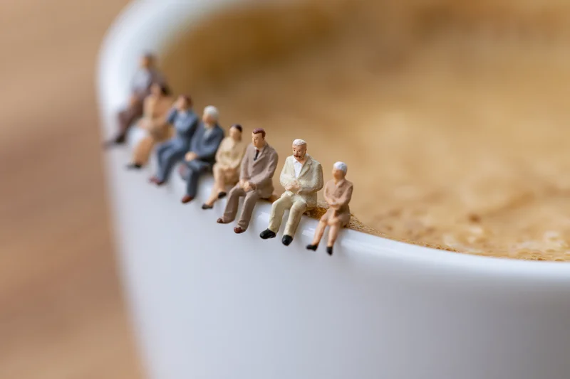 Miniature businesspeople seated in a row along the edge of a white coffee cup