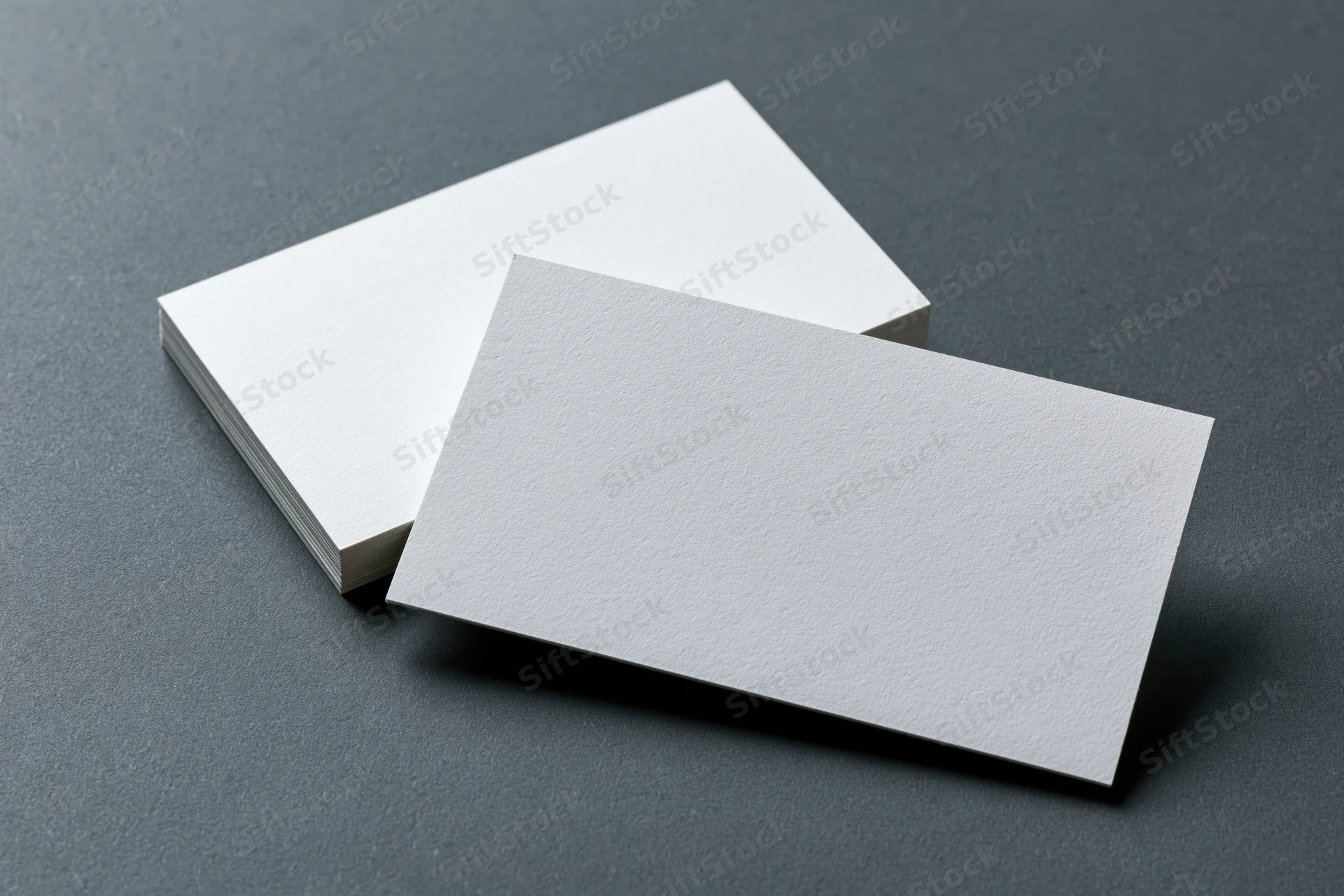 Two blank white business cards arranged at slight angles on a dark gray surface