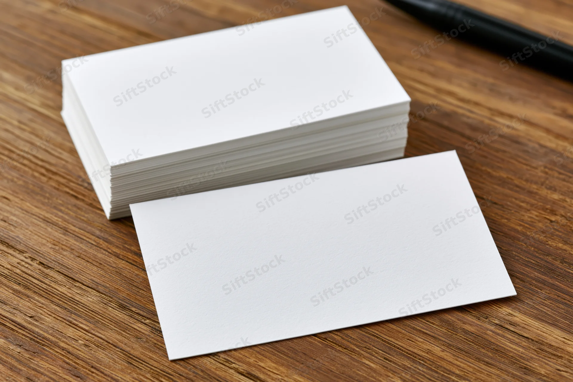 Blank white business cards arranged on wooden desk surface with one card in front and a pen nearby