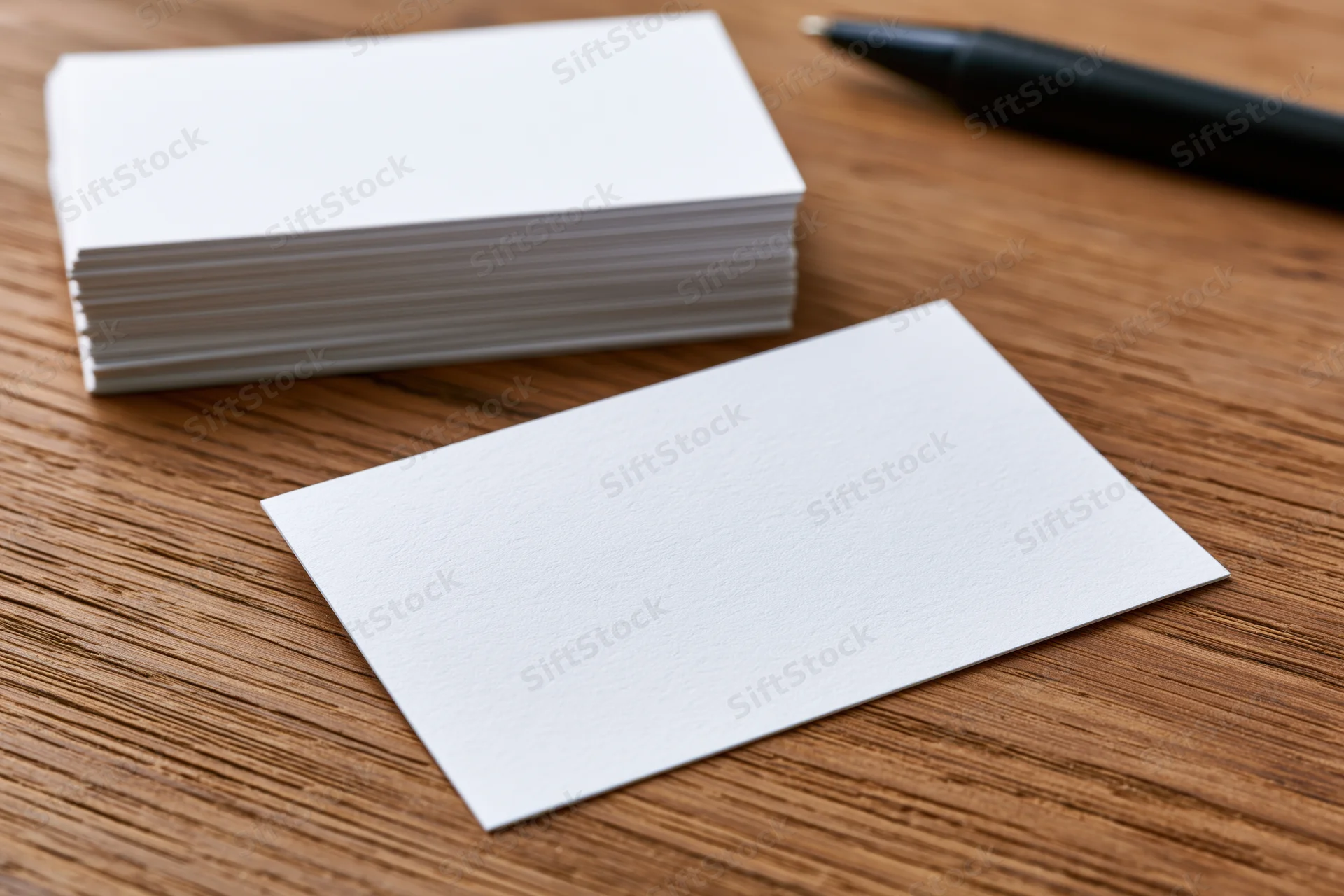 Blank white business cards arranged on a wooden desk surface with a pen nearby