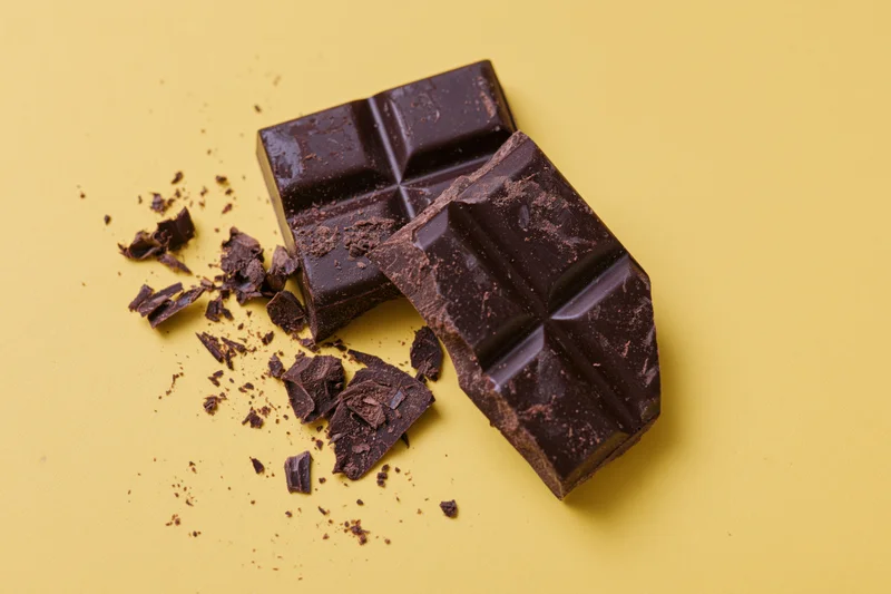 Broken dark chocolate bar pieces scattered with crumbs on yellow background
