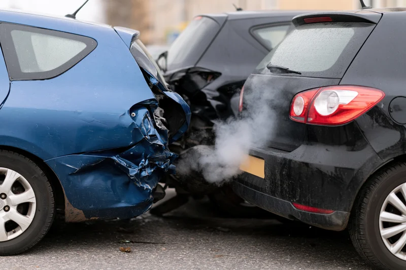 Two hatchbacks involved in a rear-end collision on asphalt road with visible damage and smoke from exhaust