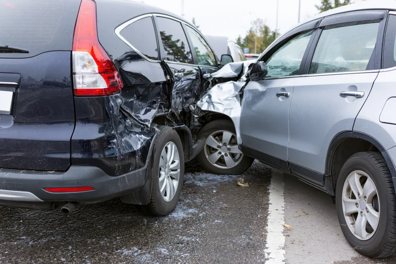 Two cars involved in a rear-end collision on a roadside with visible damage to bumpers and sides