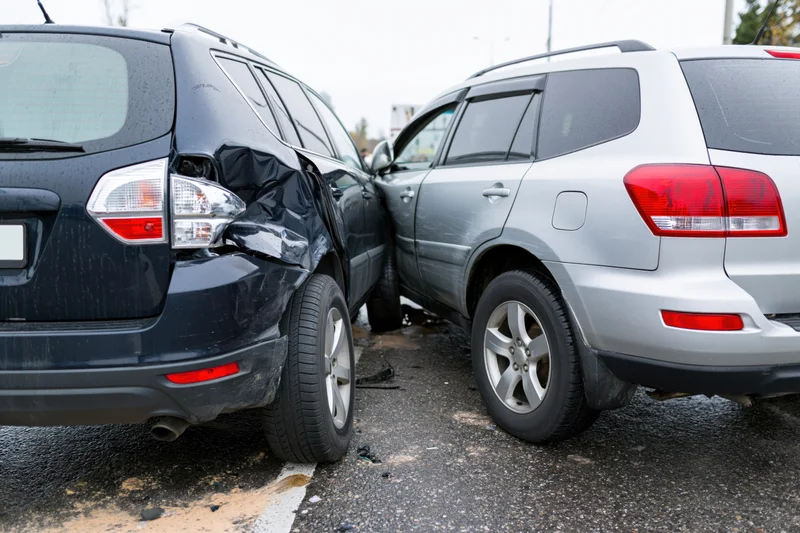 Two suvs involved in a rear-end collision on a wet roadside asphalt surface
