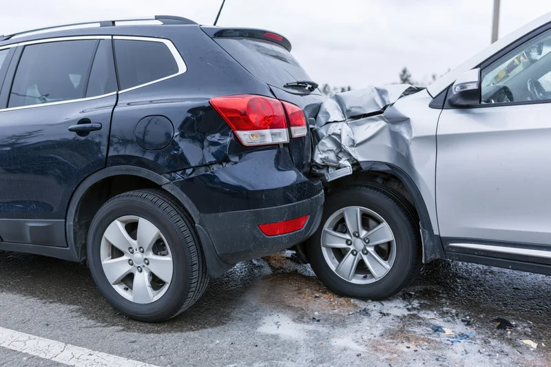 Two cars involved in a rear-end collision on a roadside with visible damage and debris on asphalt