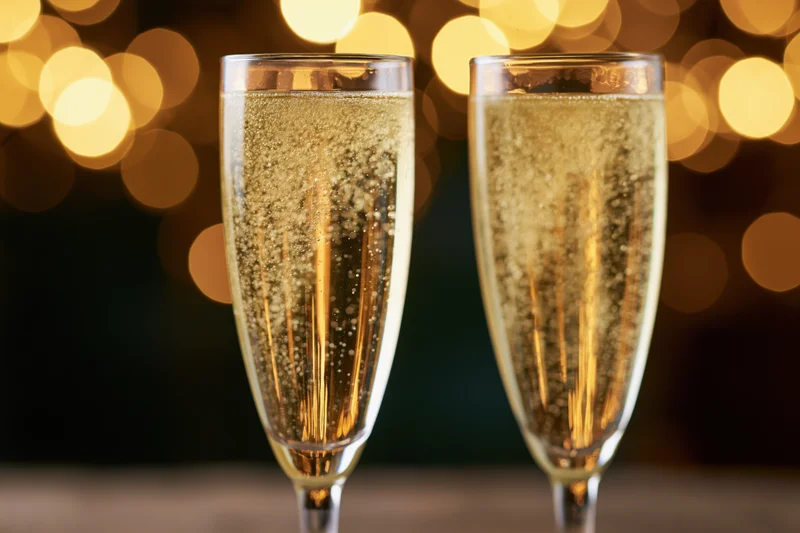 Two champagne flutes filled with sparkling wine bubbles rising against a warm bokeh light background