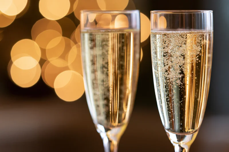 Two champagne flutes filled with sparkling wine bubbles rising against a golden bokeh background