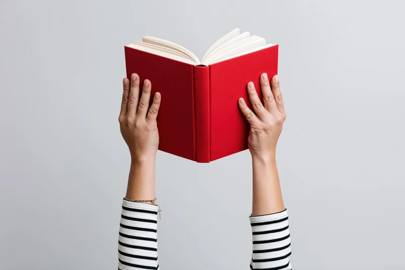 Hands holding open red hardcover book against plain background