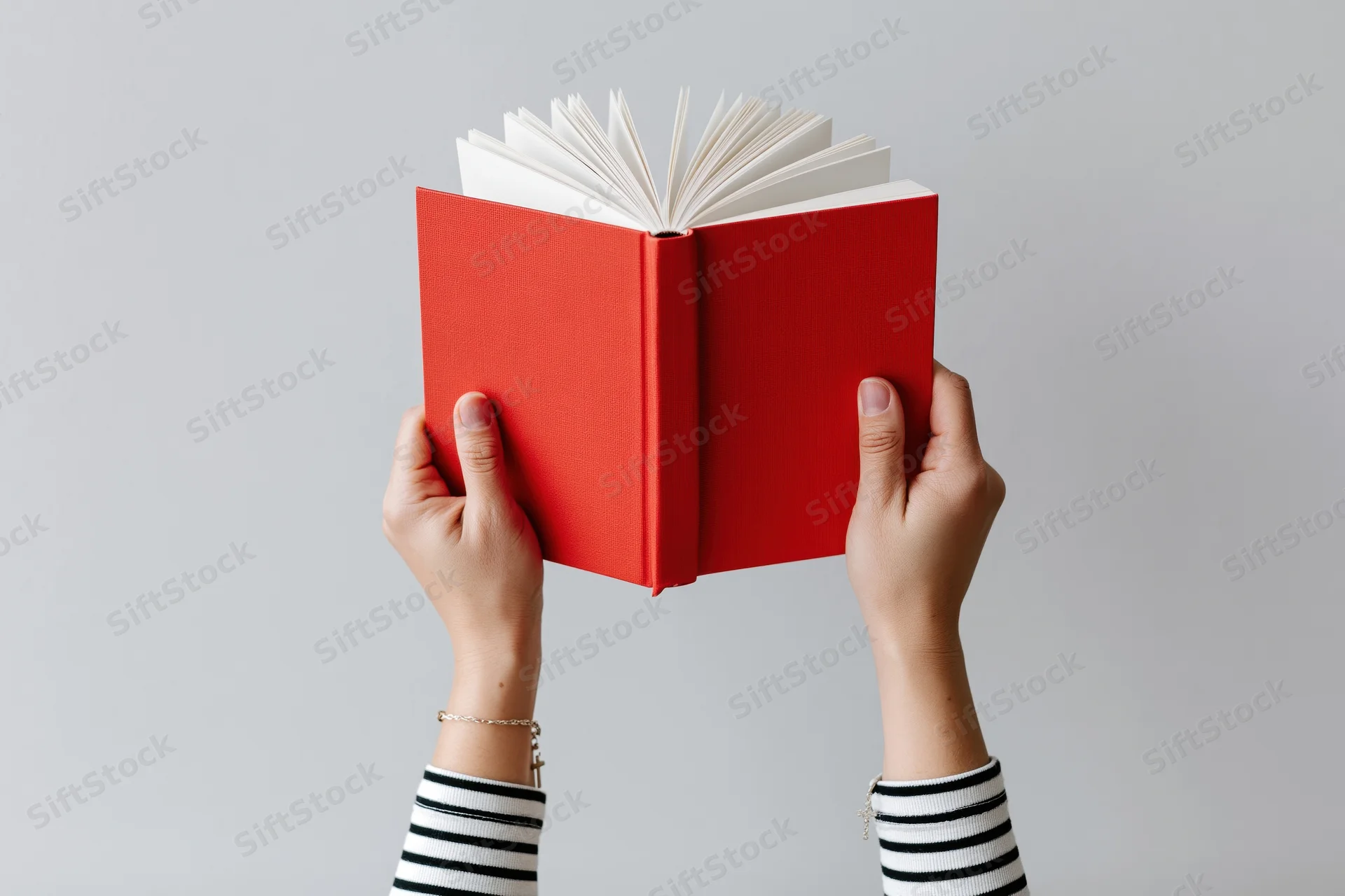 Hands holding open red hardcover book upward against plain background