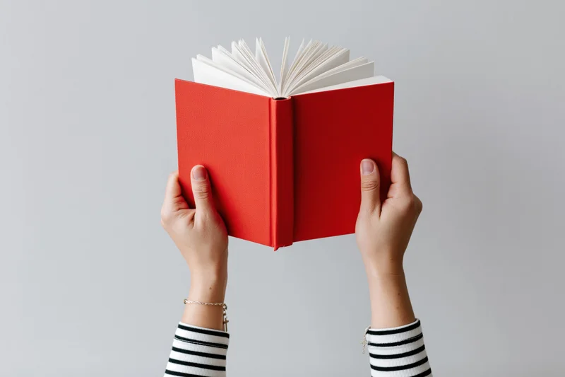 Hands holding open red hardcover book upward against plain background
