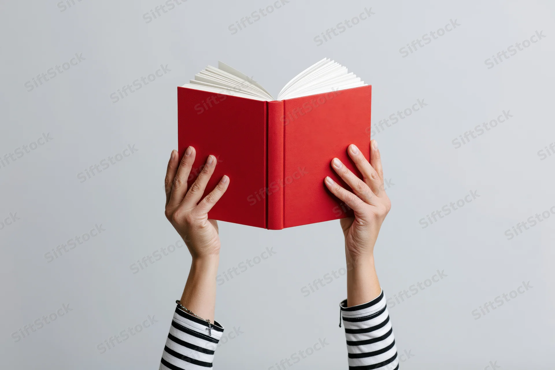Hands holding open red hardcover book against plain background