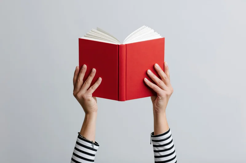 Hands holding open red hardcover book against plain background