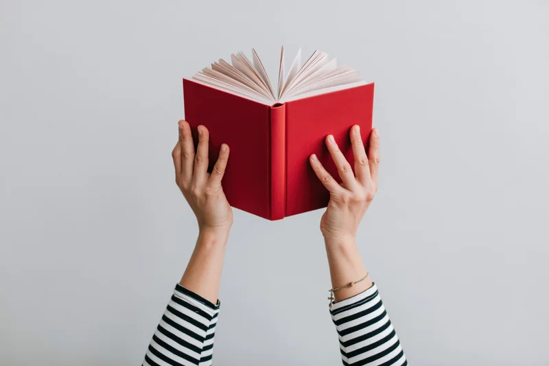 Hands holding open red hardcover book against white background